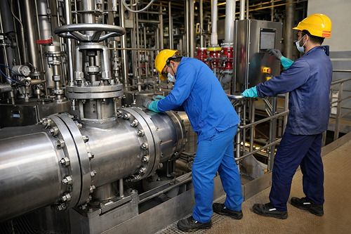 Industrial technicians monitoring valve and flange inside a modern chemical manufacturing plant